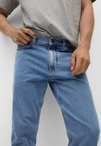 Jeans in denim azzurro chiaro con taglio a gamba dritta, dotati di chiusura con bottoni, cinque tasche e leggero scolorimento sul tessuto.