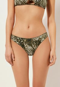 Bikiniunderdel med ett grönt och krämfärgat djurmönster, tillverkad av mjukt tyg med låg midja och sömlös midjeband.