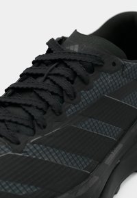 Chaussure de sport noire avec tige texturée, lacets foncés et motif design. La semelle est robuste, idéale pour l'adhérence.