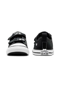 Zapatillas de lona negras con suelas de goma blanca, con dos correas de velcro y la clásica marca Converse All Star en el talón.