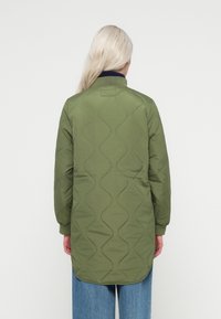 Zaļa piešūta jaka ar noapaļotu apakšu un ribinātu tumši zilu apkakli, kas izceļas ar gludu tekstūru un garām piedurknēm.