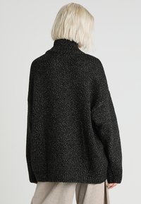 Black knitted sweater with a high collar, featuring a loose fit and textured pattern. The fabric has a subtle shimmer.