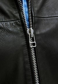 Black leather jacket featuring a silver metal zipper, revealing a blue fabric underneath. Textured surface with visible stitching detail.