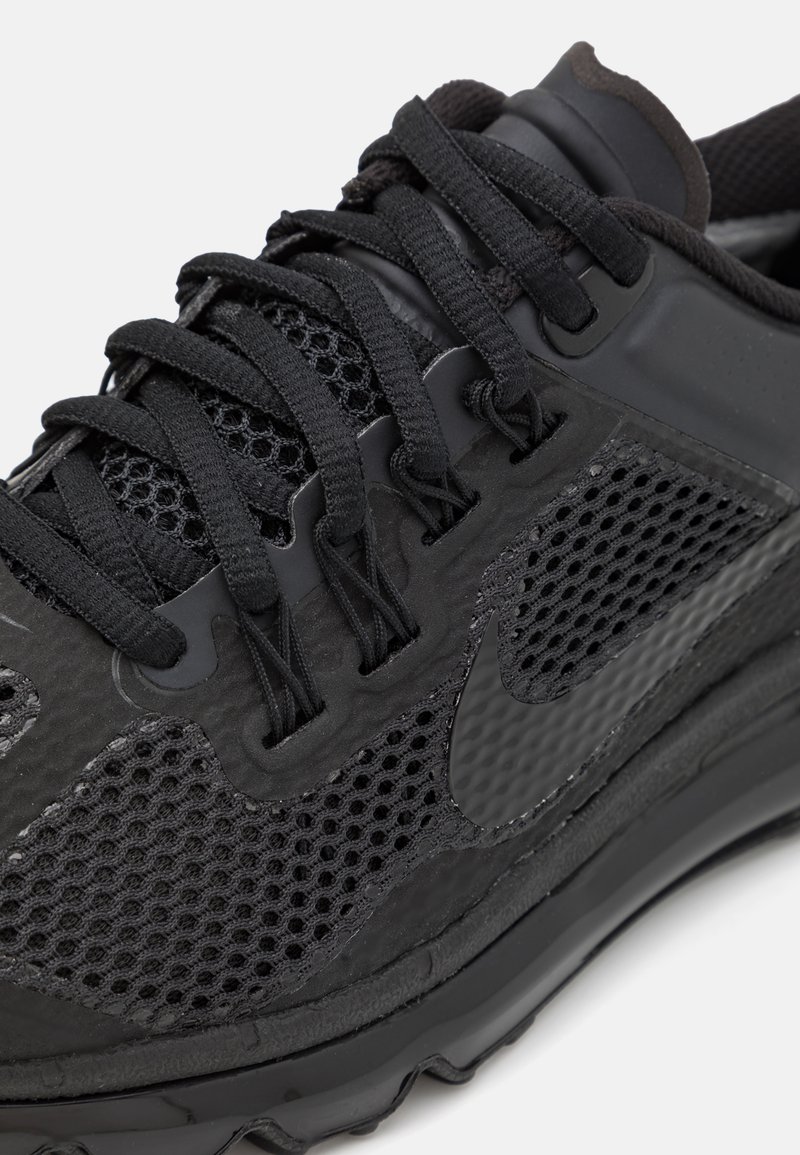 Chaussure de sport noire avec un dessus en mesh et des accents texturés, des lacets plats et une semelle en caoutchouc, avec un logo affiché sur le côté.