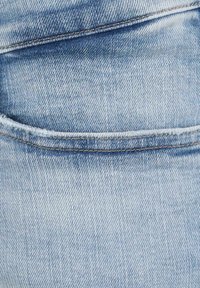 Ljusblå denimtyg med en slät yta, som har konturer av en bakficka och subtil blekning längs sömmarna.