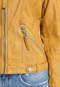 Gul läderjacka med en dragkedjeficka, texturerad yta och detaljerad sömnad. Åtföljd av urtvättad denim.