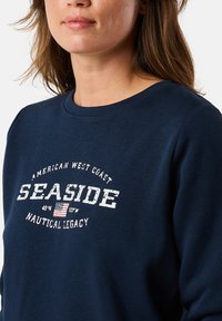 Marineblauw sweatshirt met ronde halslijn, voorzien van witte tekst "SEASIDE" en nautische graphics. Zachte stof met een minimale textuur.