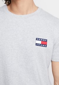 Šedé bavlněné tričko s malou obdélníkovou nášivkou loga Tommy Jeans v modré, červené a bílé barvě na levém prsu.