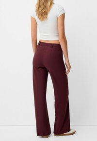 Vida byxor i en djup bordeauxfärg. Tillverkad av slätt tyg, med medelhög midja och standard bakfickor.