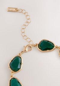 Gold chain necklace featuring multiple green teardrop-shaped stones with a polished finish. Includes a lobster clasp and adjustable links.