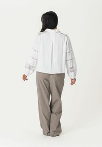 White blouse with lace detailing on sleeves, paired with loose, light brown trousers. The blouse has a pleat at the back and a round collar.