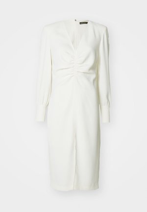 White dress with long sleeves, a deep V-neck, ruched detailing at the front, and a slit at the bottom. Smooth texture and fitted design.