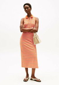 Sukienka bez rękawów w paski w kolorze pomarańczowym i białym, z kołnierzykiem i guzikami. Do tego lekka beżowa torebka i płaskie sandały.