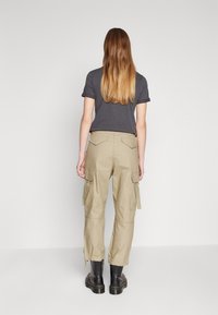 Grå kortärmad t-shirt kombinerad med ljus beige cargobyxor. Byxorna har sidofickor och en avslappnad passform, kompletterade med svarta kängor.