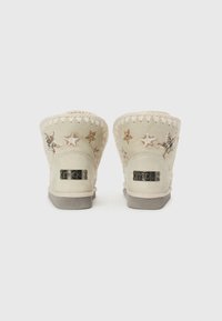 Hvide ruskinds ankle boots med broderede stjernesymbolet, syede kanter og en metallisk logo-plade på en grå gummisål.