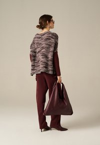 Poncho lavorato a maglia con motivo grigio e bordeaux, abbinato a pantaloni bordeaux e una grande borsa in pelle bordeaux. Gli accessori includono occhiali da sole e orecchini.