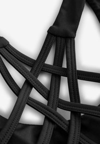 Reggiseno sportivo nero con spalline sovrapposte, realizzato in un materiale elastico morbido, con cuciture piatte e un design geometrico a incrocio.
