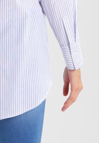 Camisa de botones a rayas en azul claro y blanco. Hecha de algodón, cuenta con mangas largas con puño, dobladillo curvado y un corte relajado.