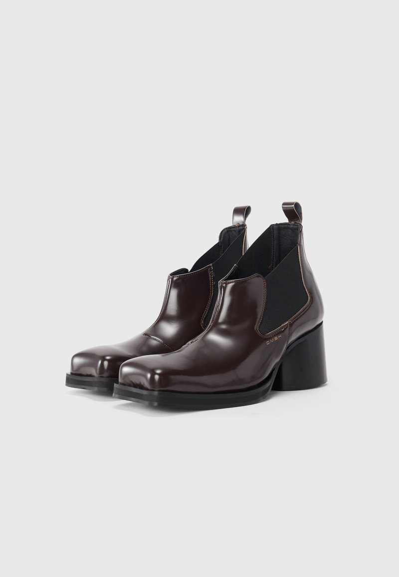 Bottes Chelsea en cuir marron avec une finition brillante, des panneaux latéraux élastiques et un talon épais noir. Design à bout rond avec des languettes.