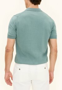 Korte mouwen polo in licht teal katoen met een klassieke kraag. Bevat ribgebreide manchetten en zijsplitten. Gladde, gestructureerde afwerking.