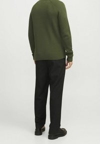 Zelený žebrovaný svetr s dlouhými rukávy, nošený s černými kalhotami a černými botami. Texturovaná tkanina s volným střihem a kulatým výstřihem.