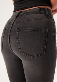 Czarne dżinsy o dopasowanym kroju, z dwiema tylkimi kieszeniami i subtelnymi detalami w szwach. Materiał ma gładkie, lekko teksturowane wykończenie.