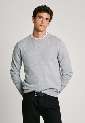 Suéter de punto gris con cuello redondo, puños y dobladillo acanalados, combinado con jeans negros y un cinturón negro, con una hebilla plateada.