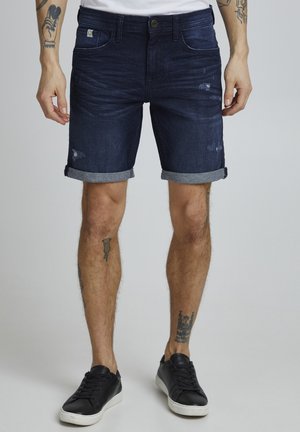 Mørkeblå denimshorts med et slidt finish, opsmøgede kanter og fem lomme-design. Bæres med sorte sneakers.