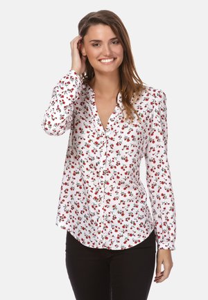 Camicia bianca con bottone, caratterizzata da un motivo floreale rosso, maniche lunghe, colletto e orlo curvo. Abbinata a pantaloni neri.