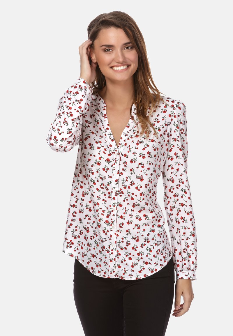 Weißes Hemd mit Knöpfen, das ein rotes Blumenmuster aufweist, lange Ärmel, einen Kragen und einen abgerundeten Saum hat. Kombiniert mit schwarzen Hosen.