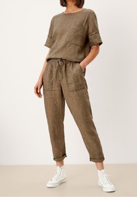 Bruine linnen top met korte mouwen en een zak, gecombineerd met elastische taillebroeken en witte sneakers. Casual fit; de stof is los en ademend.