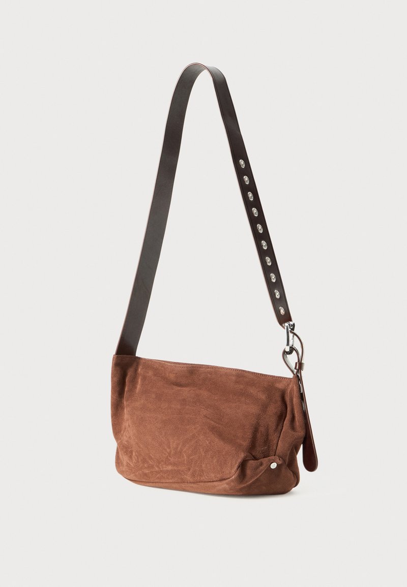 Brown suede shoulder bag with a smooth surface, a dark leather strap featuring silver studs, and a rounded, unstructured shape.
