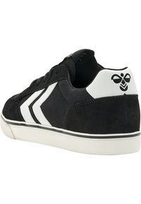 Schwarze Leinensneaker mit weißer Gummisohle, mit einem weißen Chevron-Design und Logo-Akzenten an der Ferse. Weicher Wildledertextur im Obermaterial.