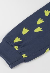 Manica di tessuto blu navy con polsino a costine e forme astratte di colore verde lime sparse che ricordano impronte stilizzate di uccelli.