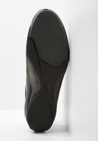 Semelle de basket noire avec caoutchouc texturé pour l'adhérence, design élégant aux bords courbes, et marquage subtil embossé sur le côté.