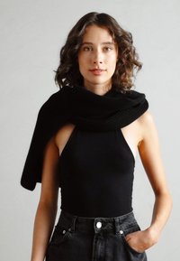 Bodysuit negro sin mangas con un escote alto, combinado con unos pantalones cortos de mezclilla negros de cintura alta. Bufanda negra de punto drapeada sobre los hombros.