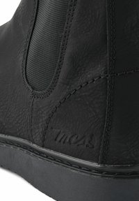 Bota de cuero negro con paneles laterales elásticos, material texturizado y una suela oscura contrastante con costuras decorativas y marca.
