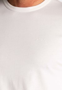 Witte katoenen t-shirt met een ronde hals, voorzien van een klein embossed logo op de borst. Zachte textuur en slanke snit.