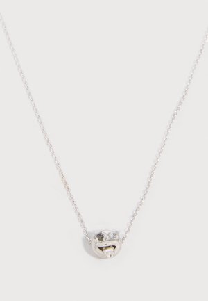 Silver chain necklace with a small silver pendant shaped like a smiley face, featuring black and white stone eyes and a tongue sticking out.