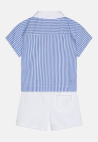 Chemise à manches courtes avec des rayures bleues et blanches, col blanc ; associée à un short blanc avec une poche arrière. Matériau en coton doux.