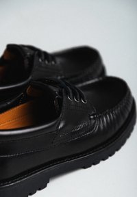Scarpe in pelle nera con punta tonda, design con lacci e cuciture visibili. Presentano una suola nera testurizzata e un interno arancione a contrasto.