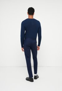 Camisa de malha de manga longa azul marinho combinada com calças justas azul marinho e sapatos pretos. O top apresenta um decote redondo e punhos ajustados.