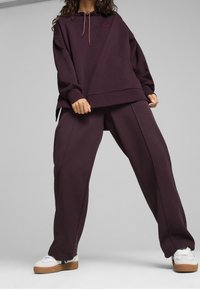 Felpa oversize di colore viola scuro con cordoncino, abbinata a pantaloni larghi viola scuro. Sneakers bianche con suola color gomma completano l'outfit.