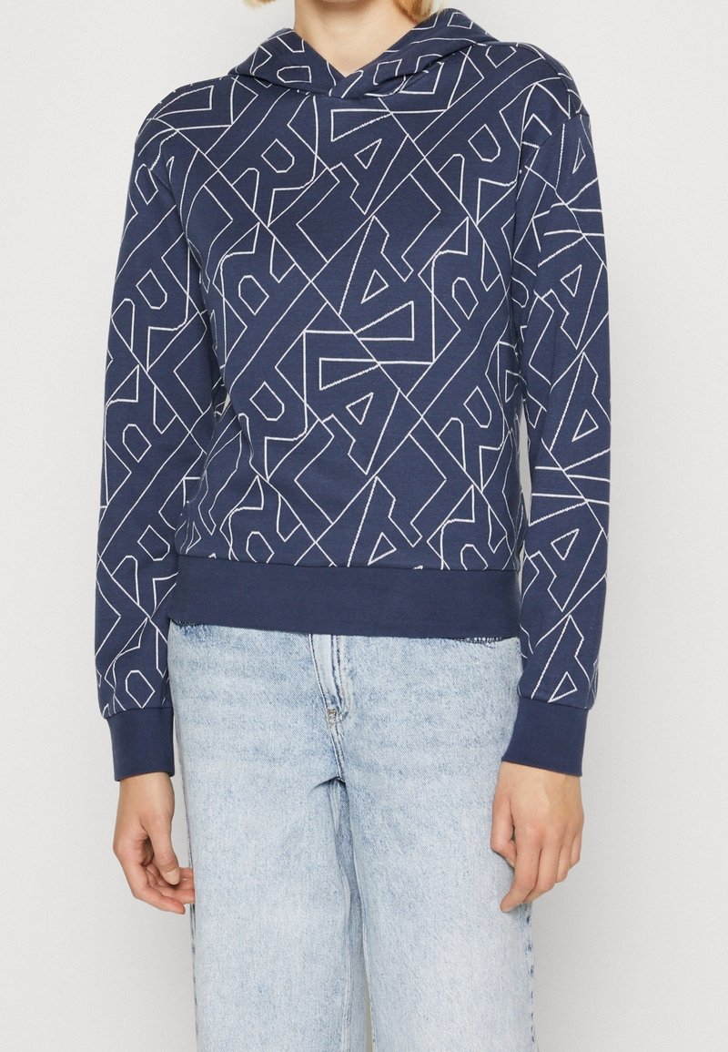 Marinblå hoodie med ett geometriskt vitt mönster, mjukt tyg, långa ärmar, en framficka och en avslappnad passform med ribbade ärmslut.