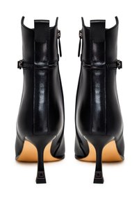 Bottes basses en cuir noir avec talons carrés fins, fermetures éclair à l'arrière et languettes de retrait, vues de dos sur fond blanc.