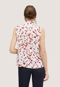 Blusa senza maniche in tessuto bianco con un motivo a cuori rossi e viola sparsi. Presenta un colletto alto e un orlo dritto sul retro.