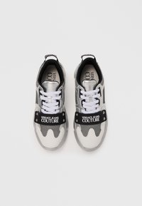 Versace Jeans Couture-sneakers har en metallisk sølvfarge på overdelen, nettingpaneler, hvite snører og en svart logostropp over midtfoten.