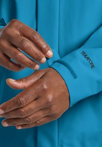Giacca impermeabile blu con polsini regolabili tramite velcro. Il tessuto appare liscio, con un logo ben visibile che recita "TEXAPORE" vicino al polsino.