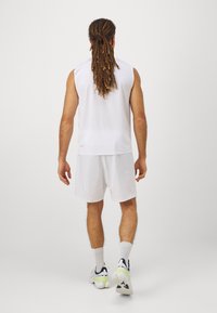 Top sem mangas branco e calções, feitos de tecido leve. Detalhes notáveis incluem uma textura suave e um design minimalista.