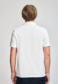 Biała koszulka polo, krótkie rękawy, bawełniany materiał, klasyczny kołnierzyk, czysty design, brak widocznych logo czy wzorów, gładki widok z tyłu.